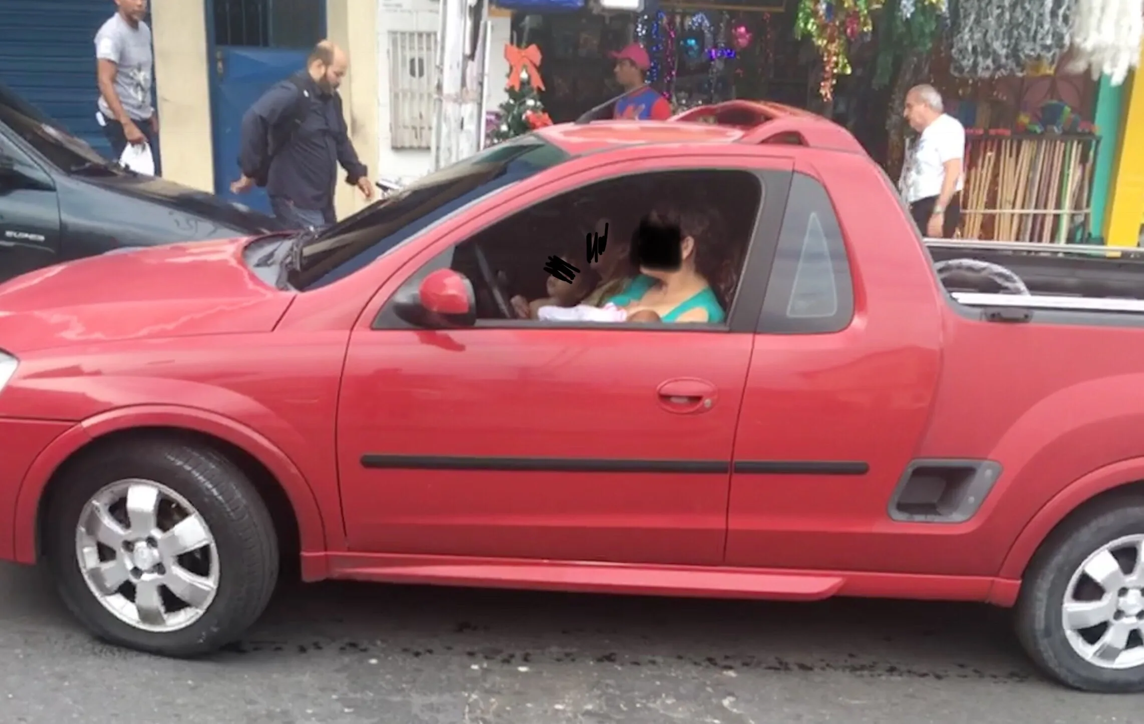 Além de dirigir e amamentar, percebe-se na foto que há outra criança no colo de um adulto no banco do passageiro.